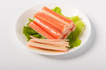Crab sticks made of crab meat are placed on lettuce leaves, in delicate plates, isolated in white background