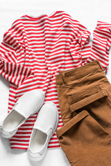 Women's cotton t- shirt with red stripes, corduroy brown banana jeans and white sneakers on a light background, top view