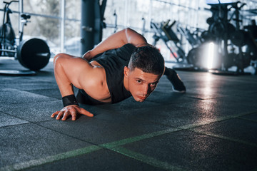 Fototapeta na wymiar Strong young man in sportive clothes doing push ups in gym