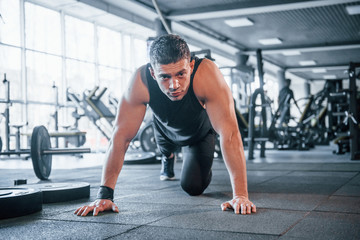 Fototapeta na wymiar Strong young man in sportive clothes doing push ups in gym
