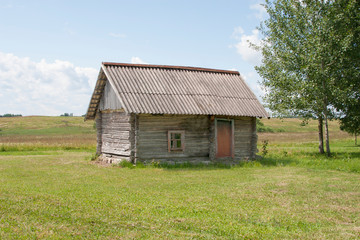 Fototapeta na wymiar small little old wooden raster log hut in the middle field near by birch tree