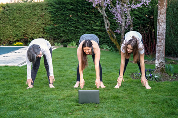 Obraz premium Mother, grandmother and teen daughter practicing fitness lesson online outdoors in garden at quarantine isolation period during coronavirus pandemic. Family doing sport together at home via skype