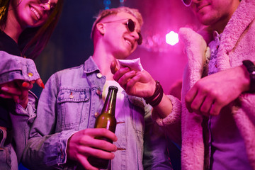 Buying drugs. Young people is having fun in night club with colorful laser lights