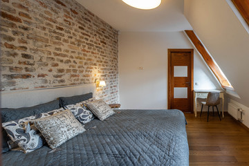 Modern contemporary loft interior of bedroom. Brick wall. Cozy bed with pillows. Sloping ceiling.