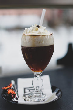 Closeup of delicious glass of Irish Coffee with heavy cream on top. High aperture, ski resort in the background. St Anton am Arlberg ski resort, Austria, Europe -Image