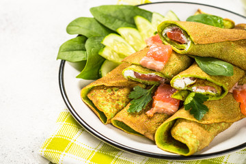 Green pancakes from spinach wrapped with salmon and cream cheese.