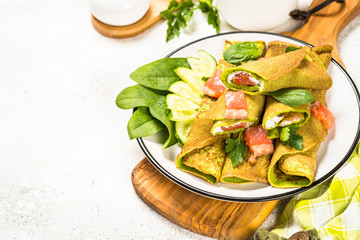 Green pancakes from spinach wrapped with salmon and cream cheese.