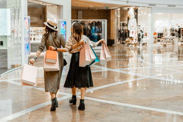 Shopping and entertainment, mall inside. Two beautiful girls with paper bags at the mall. The joy...