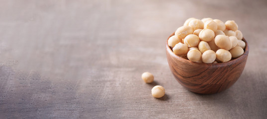 Macadamia nuts in wooden bowl on wood textured background. Copy space. Superfood, vegan, vegetarian food concept. Macro of macadamia nut texture, selective focus. Healthy snack.