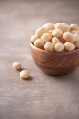 Macadamia nuts in wooden bowl on wood textured background. Copy space. Superfood, vegan, vegetarian food concept. Macro of macadamia nut texture, selective focus. Healthy snack.