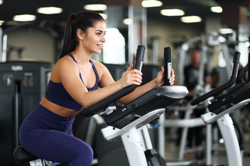 Fototapeta premium A beautiful athletic young brunette woman in sportswear in the gym is engaged on a bike.