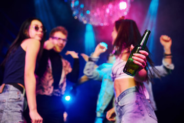 Girl holding bottle. Young people is having fun in night club with colorful laser lights