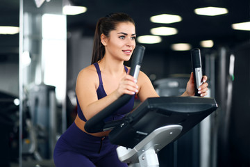 Fototapeta premium A beautiful athletic young brunette woman in sportswear in the gym is engaged on a bike.