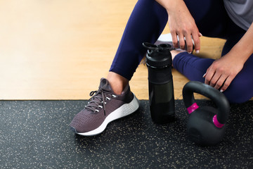 Obraz premium The concept of the gym sport. Fitness equipment. A woman sits on the floor in sneakers. A kettlebell and dumbbells.