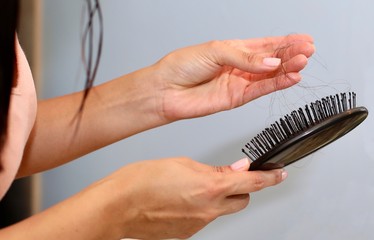 Woman pulling hair out of brush from postpartum hair loss from pregnancy.