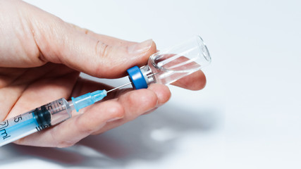 Doctor hand holds glass medicine bottle with injection fluid with blue aluminium caps and syringe for vaccination. Coronavirus epidemic, Cancer, painand diabetes, pharmaceutical medicine concept .