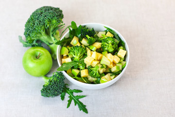plate of green salad with broccoli, apple, arugula on a gray background. Fresh, organic food for a healthy lifestyle, weight loss, detox