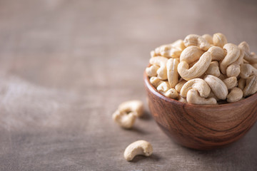 Cashew nuts in wooden bowl on wood textured background. Copy space. Superfood, vegan, vegetarian food concept. Macro of walnut texture, selective focus. Healthy snack