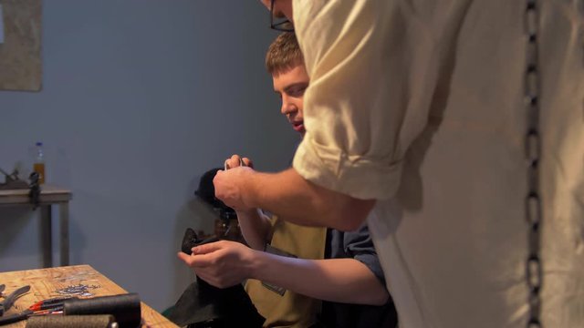 Master shows an instrument to man in the workshop