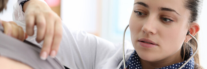 Close-up of family doctor accepting ill patient at clinical room. Young medical worker listening to...