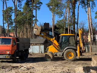 Fototapeta na wymiar Tractor and truck near the destroyed brick house. Construction machinery on the background of the ruins of the house. Demolition of an old house with an excavator. Irpin, Kiev region, March 13. 2020