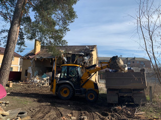 Tractor and truck near the destroyed brick house. Construction machinery on the background of the...