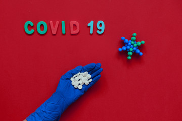 Hand in  protective glove with pills,inscription COVID 19 .Red background. Coronavirus concept. Pandemic in the world.