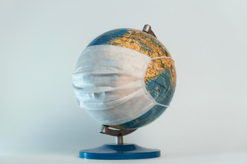 Earth globe and medical mask on white background; global pandemic covid-19, coronavirus; problems of humanity; deadly diseases