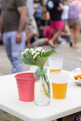 mesa evento gastronomico con vasos cerveza y flores gente al fondo