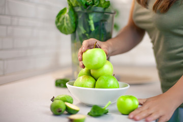 Girl takes a green apple and wants to make a detox smoothie drink. On the table is a plate of apples and greens. Fresh, organic food for a healthy lifestyle, weight loss, detox, ketone diet.
