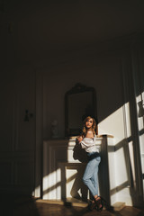 The concept of shooting in a photo Studio with hard lighting from the Windows. Sexy sensual blonde in a black hat , underwear and jeans poses for the camera in the shade on the floor of an apartment