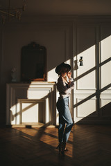 The concept of shooting in a photo Studio with hard lighting from the Windows. Sexy sensual blonde in a black hat , underwear and jeans poses for the camera in the shade on the floor of an apartment