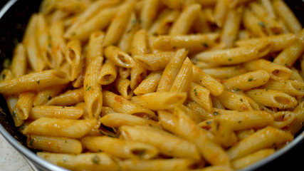 Closeup photography of Italian paste cooking in the pan with tomato basil sauce and spices. Cooking process top front view 