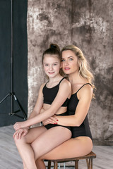 vertical portrait on a gray background of a young pretty European with a ten-year-old daughter