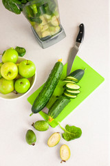 Green set of products for a healthy smoothie top view. A woman begins to cut a cucumber to make a smoothie. Morning detox for a healthy lifestyle, weight loss, ketone diet, raw food diet