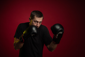 Male athlete boxer with gloves in his hands posing against a dark red background
