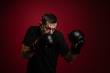 Male athlete boxer with gloves in his hands posing against a dark red background