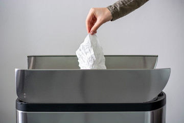 Women hand throwing a white used crumpled tissue paper into a garbage trash bin. Coronavirus advice includes use a disposable paper tissue.