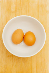 Two brown eggs isolated In a white cup on Wood background