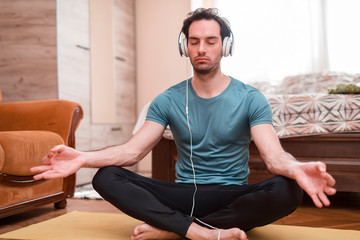 Single male with headphones doing yoga at the home, he is fit, healthy and flexible