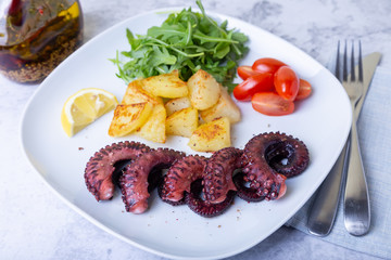 Grilled octopus with fried potatoes, arugula, tomatoes and lemon. Close-up.