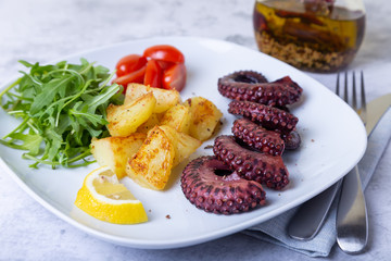 Grilled octopus with fried potatoes, arugula, tomatoes and lemon. Close-up.