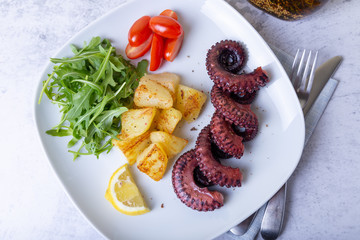Grilled octopus with fried potatoes, arugula, tomatoes and lemon. Close-up.