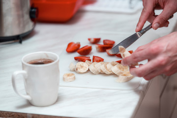 Close up look of male hands, how he preparing fruits for salad and cups of coffee in the morning at home.