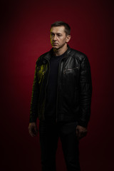 Brutal man in a black leather jacket poses against a dark red background