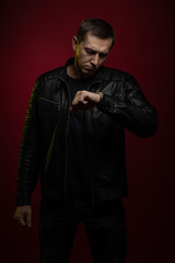 Fototapeta na wymiar Brutal man in a black leather jacket poses against a dark red background