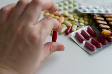  Red capsule in hand, multi-colored pills and capsules on a white background. Pills in a plastic blister. Healthcare and medicine concept.