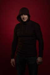 Fototapeta na wymiar A man in a jumper with a hood and with a phone in his hands poses against a dark red background