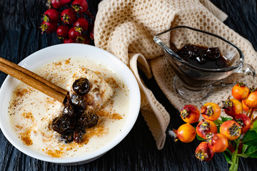 Sour-milk yogurt dessert, with thermostatic cooking, decorated with ripe cherry berries in syrup, on a dark background with jam in sauce and a stick of cinnamon, next to sprigs of fresh red berries