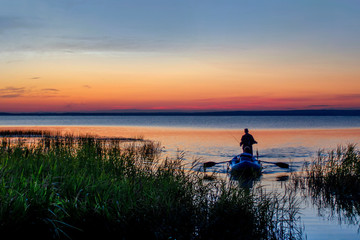 Naklejka na ściany i meble Evening fishing on the lake. Boat with fishermen on the background of a beautiful sunset.
